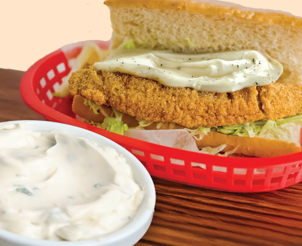 A fried fish sandwich in a basket with Mack's Tartar and Salad Dressing, and a bowl of the dressing beside it